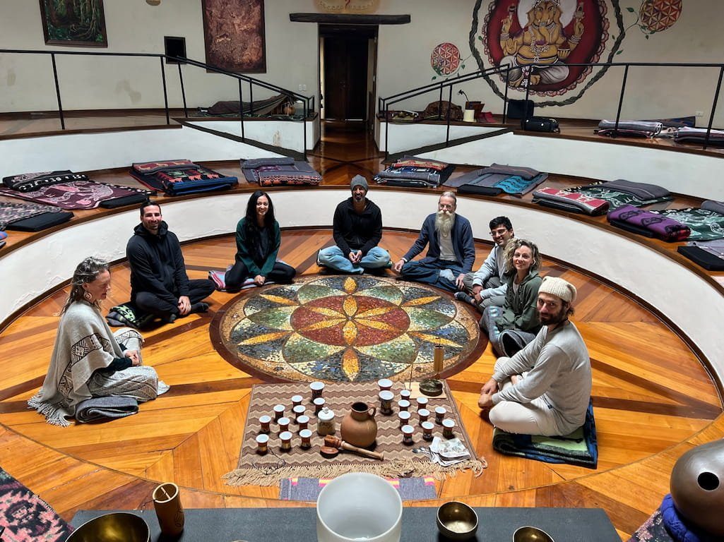 A group seated in a circle on a round floor painted with a mandala, instruments laid in the centre, a domed room around them.