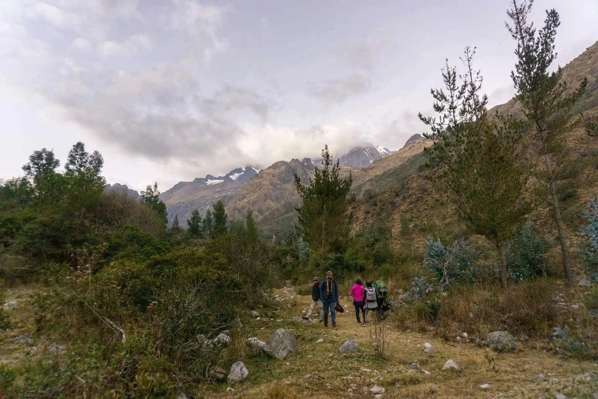 Four people standing together in a clearing below cloud covered peaks, small against the scale of the valley.
