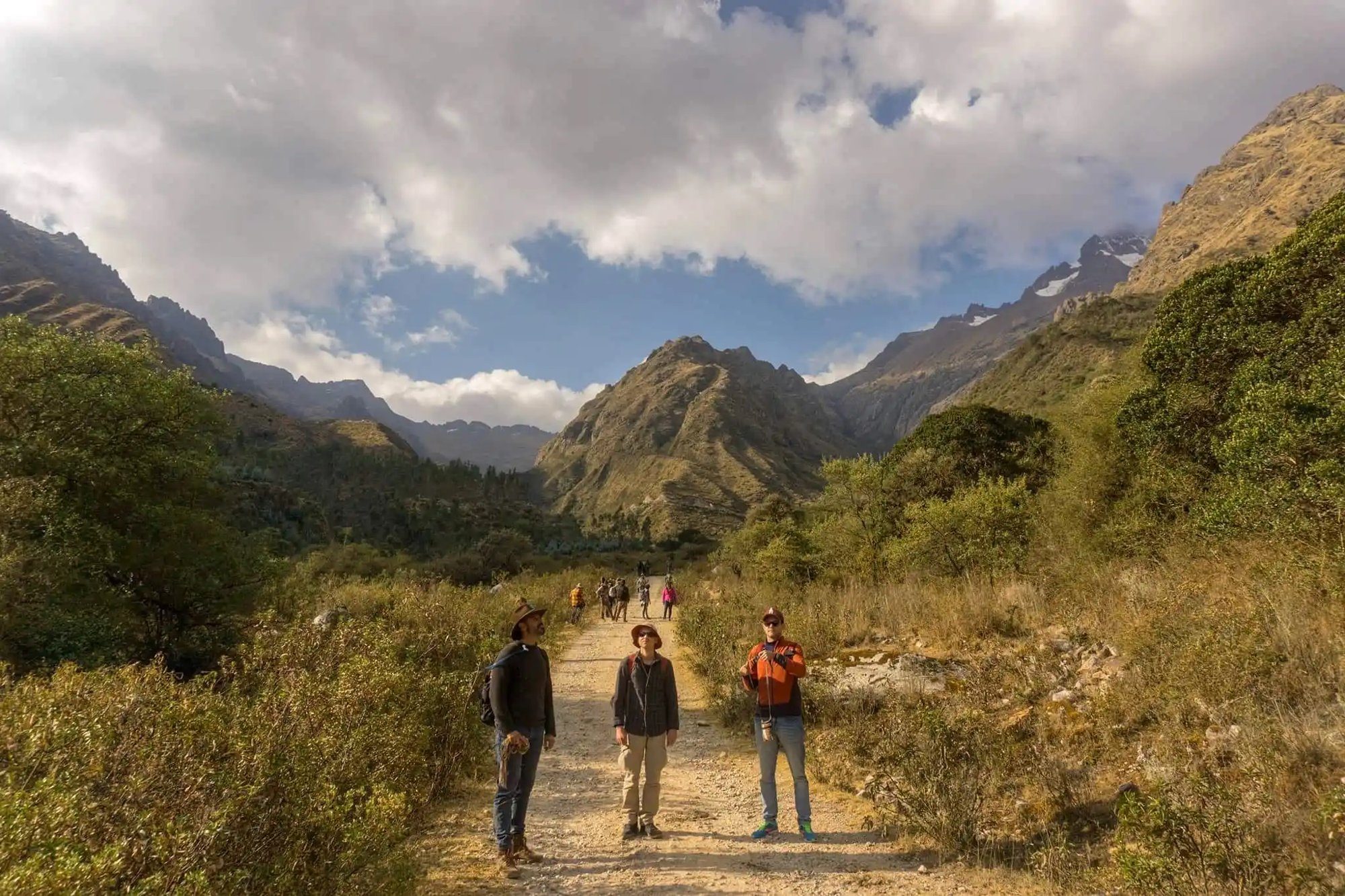 A group of five walking along a dirt road in a green valley, snow on the peaks ahead.