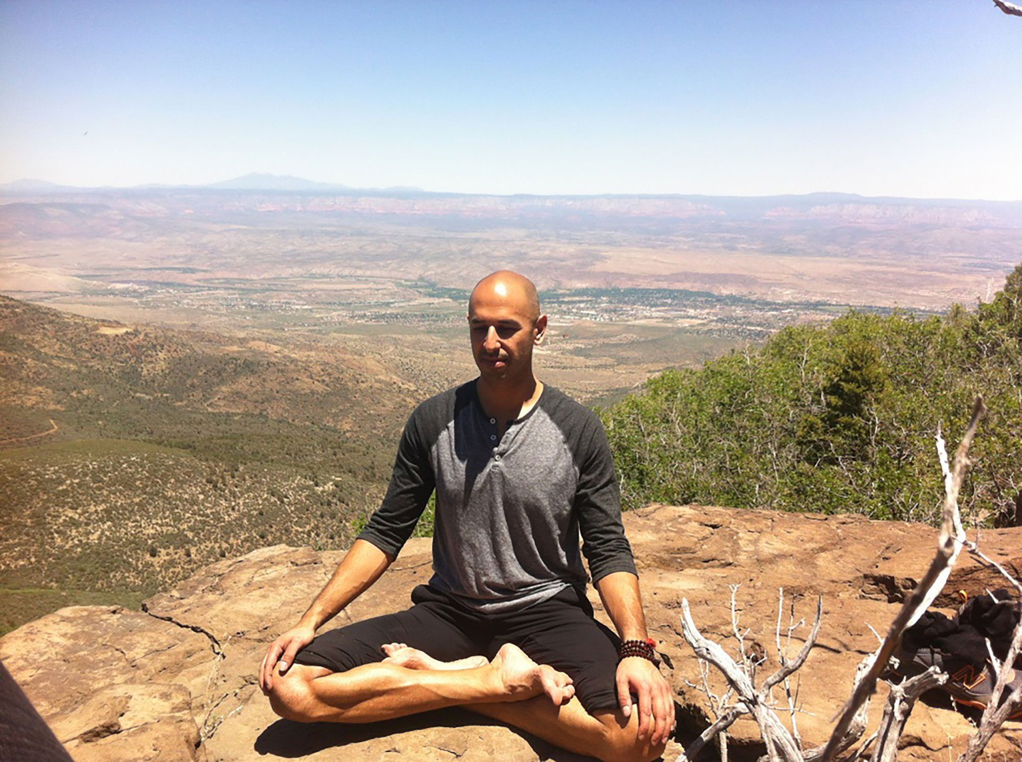 Hamid Jabbar seated cross legged on a rock at the edge of a cliff, a wide plain far below.