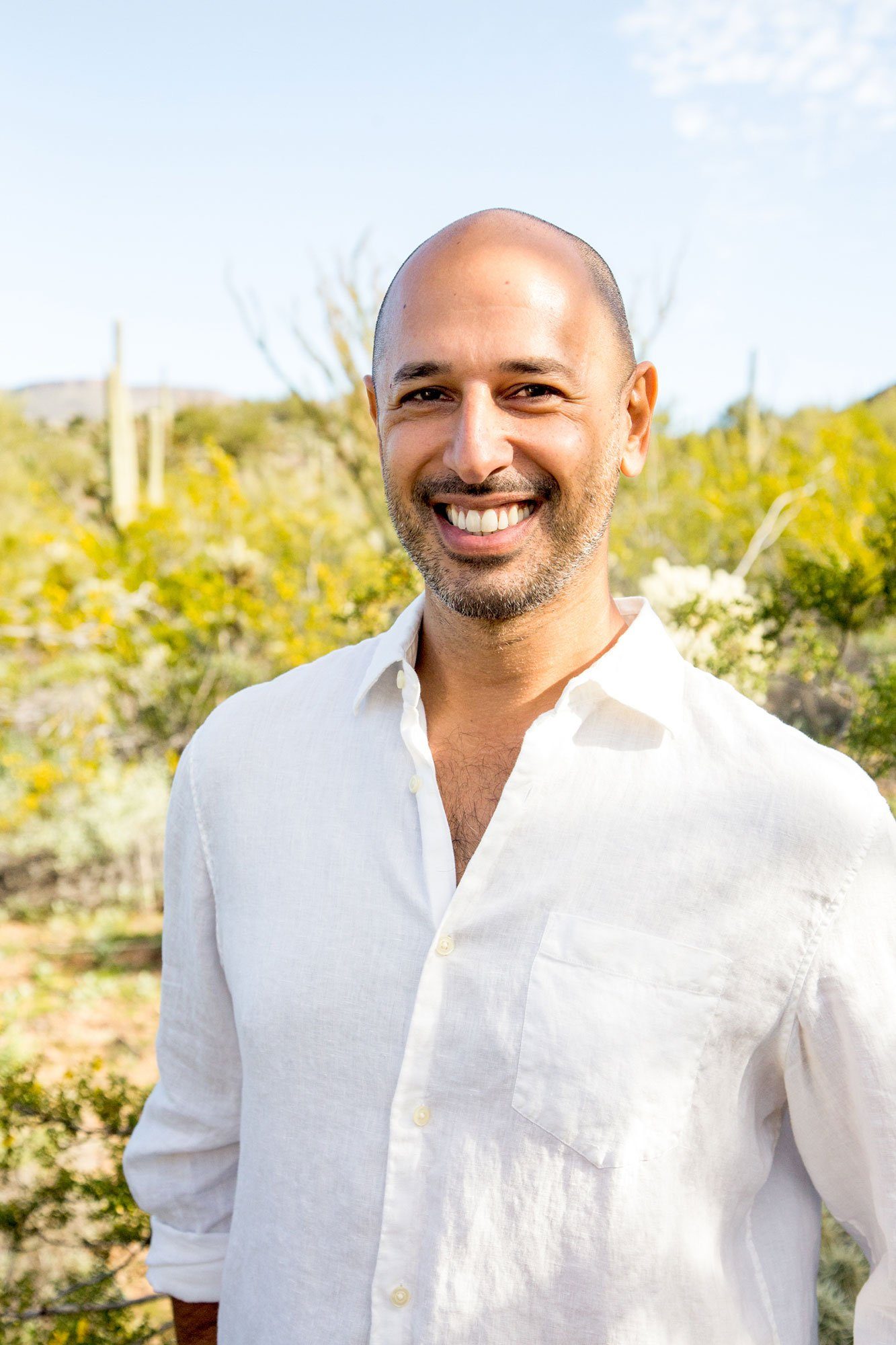 Hamid Jabbar smiling in a white shirt in front of a tall cactus and desert scrub.