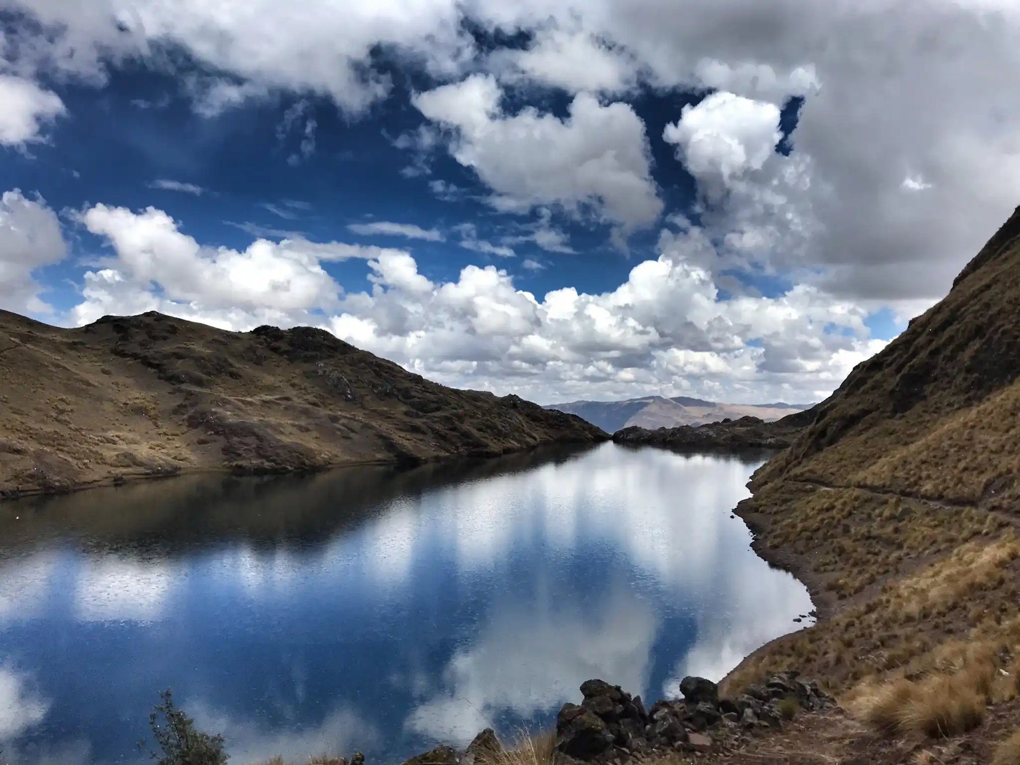 A high mountain lake under a sky of white clouds, grassland running down to the shore.