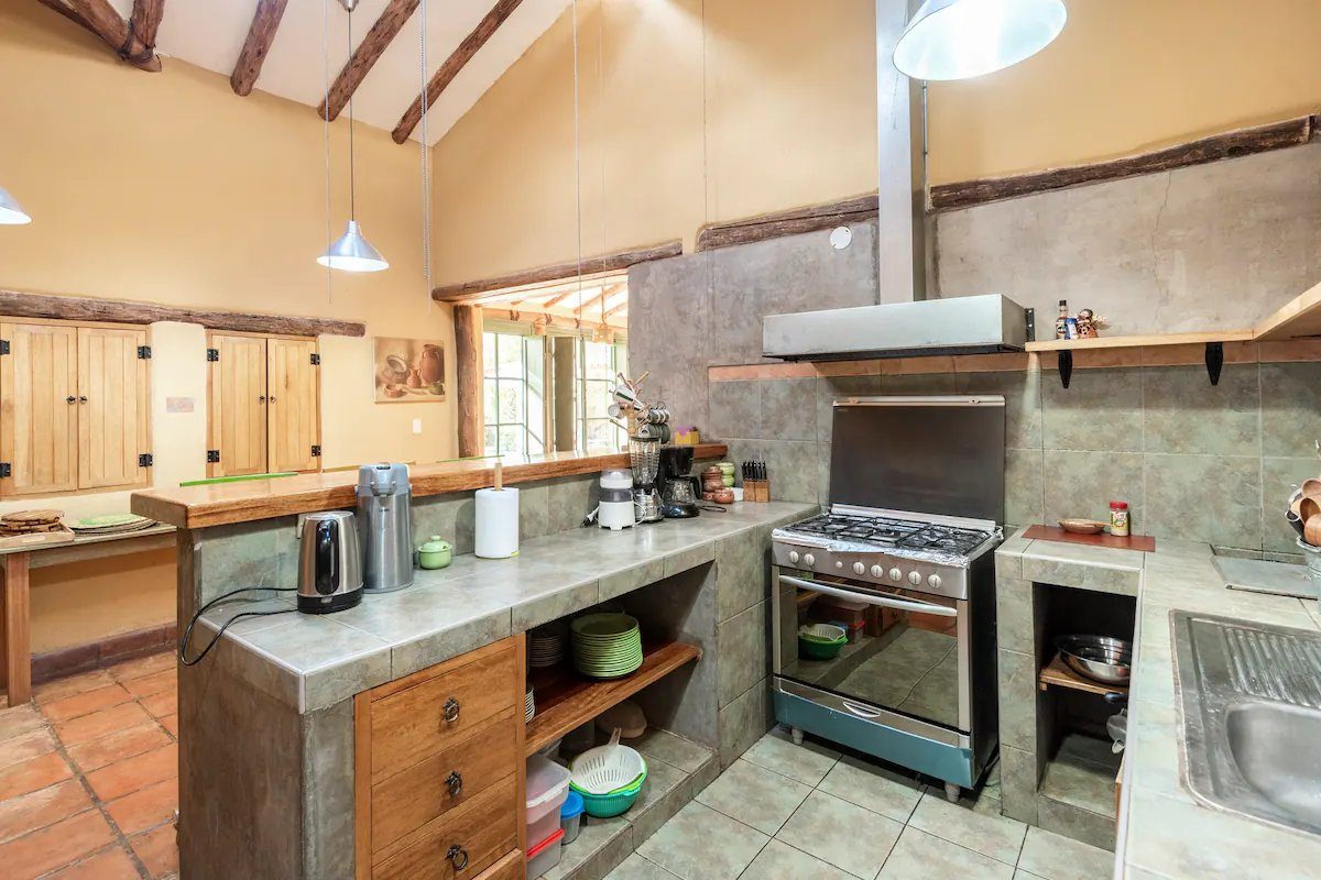 A kitchen with a concrete counter, a gas range, open wooden shelves and a window onto the garden.