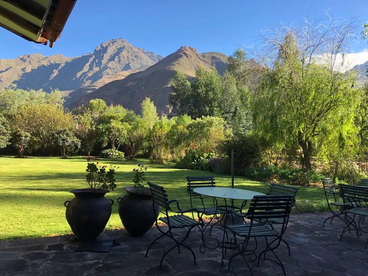 A stone terrace set with garden chairs and planted urns, looking across the lawn to the mountains.